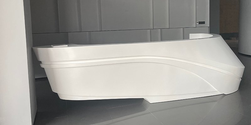 An elegant, curved reception desk made from white 100% acrylic solid surface.